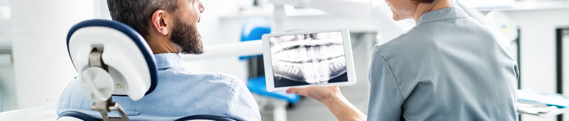 A person is seated in a dental chair, receiving care from a dental professional who stands behind them.