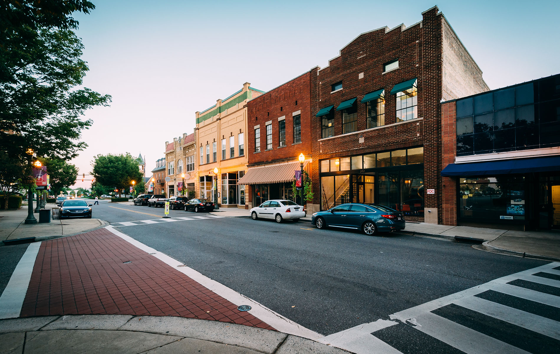 The image depicts a quiet city street at dusk, with buildings on both sides and an intersection visible.