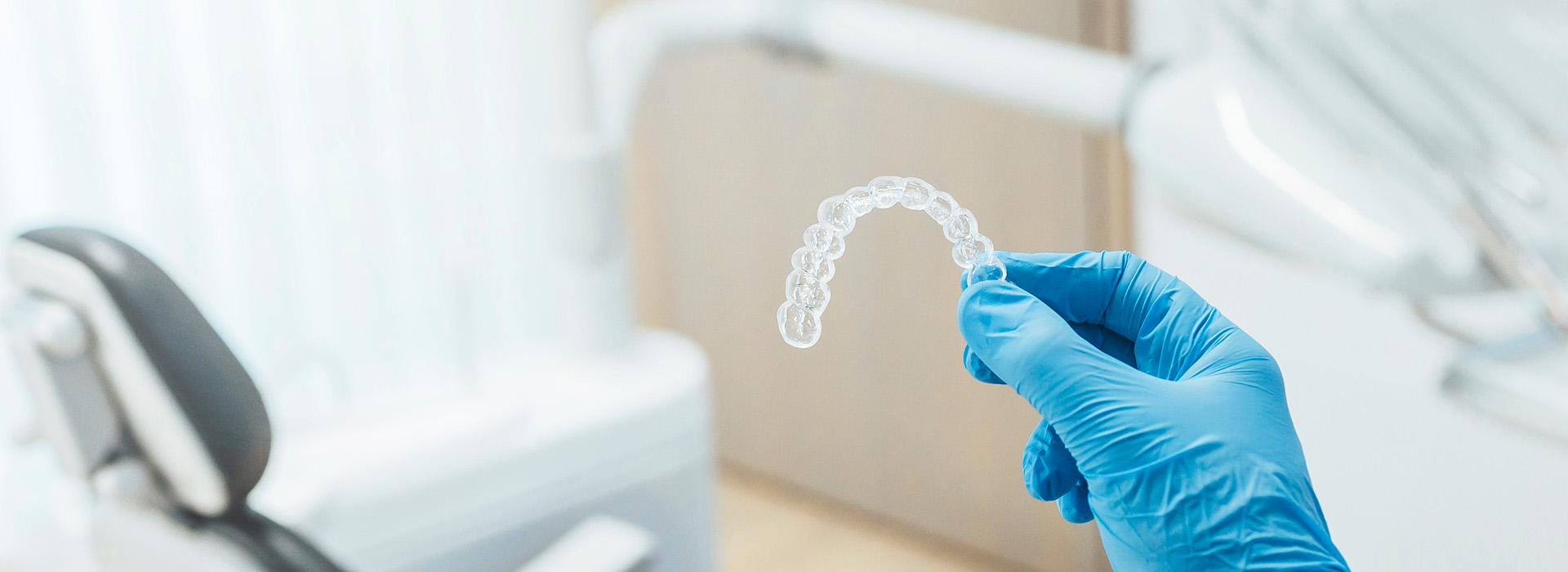 A hand holding a transparent mouthguard over a dental chair, with a focus on hygiene and safety in a dental setting.